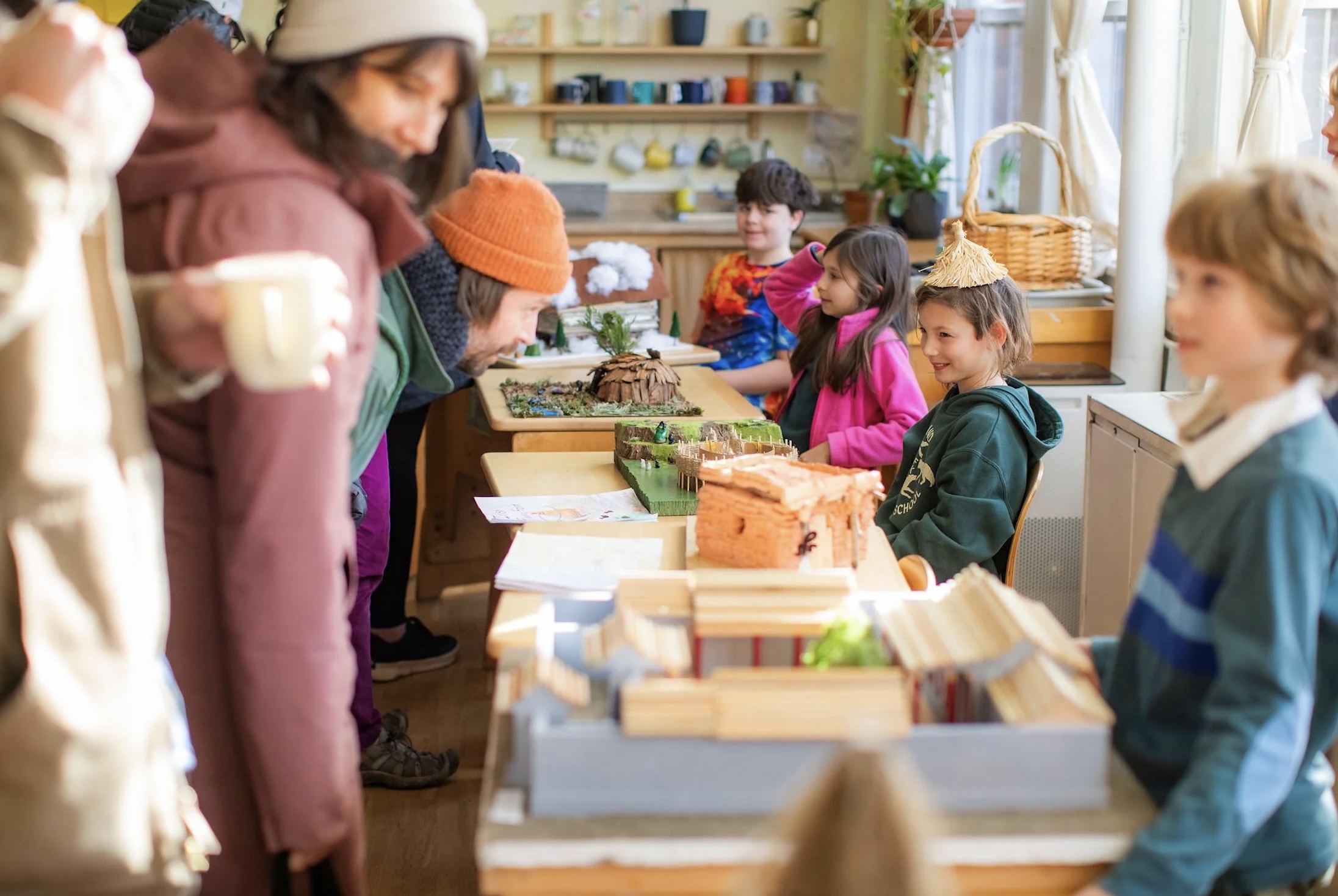 Waldorf students gathered around tables displaying handmade diorama models during a project showcase.