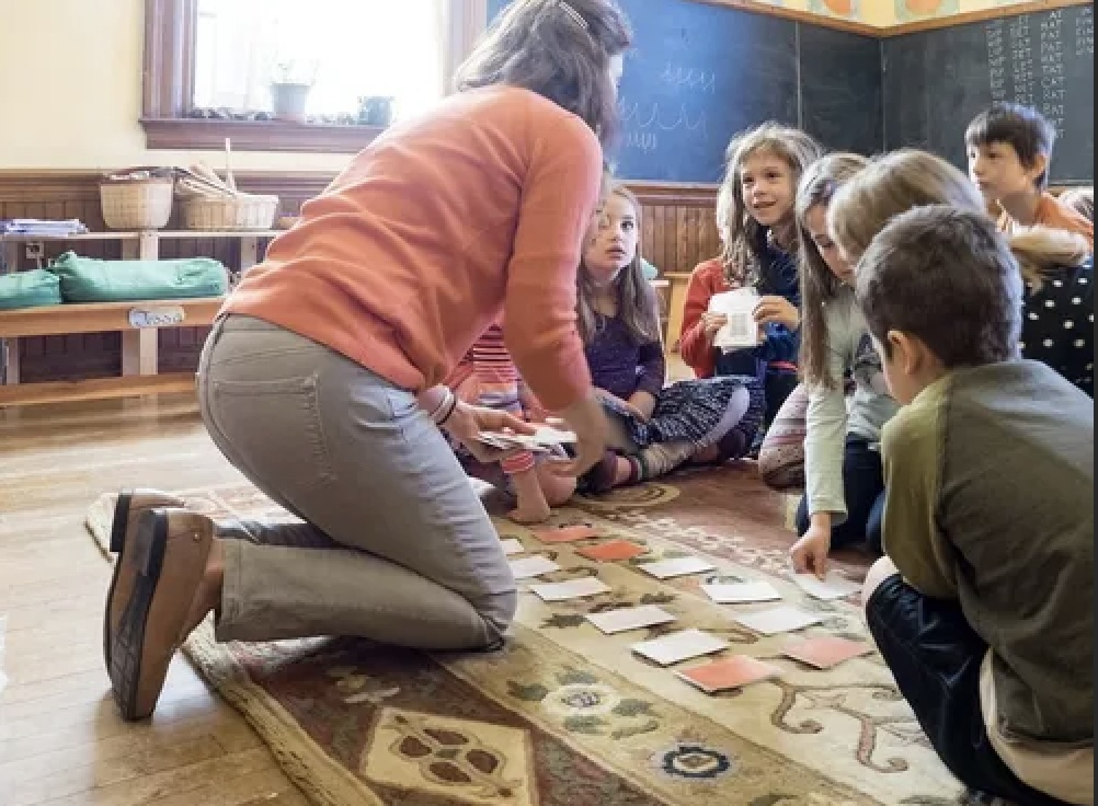 A teacher kneeling on a rug, working through a card-matching activity with a small group of young students.